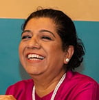Portrait of Amsa Khan and campaign ambassador seated indoors, wearing a bright pink top, associated with Stop Hunger initiatives