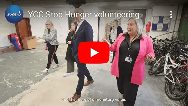 Video thumbnail showing a guided tour inside a facility with several people walking past bicycles, titled ‘YCC Stop Hunger volunteering