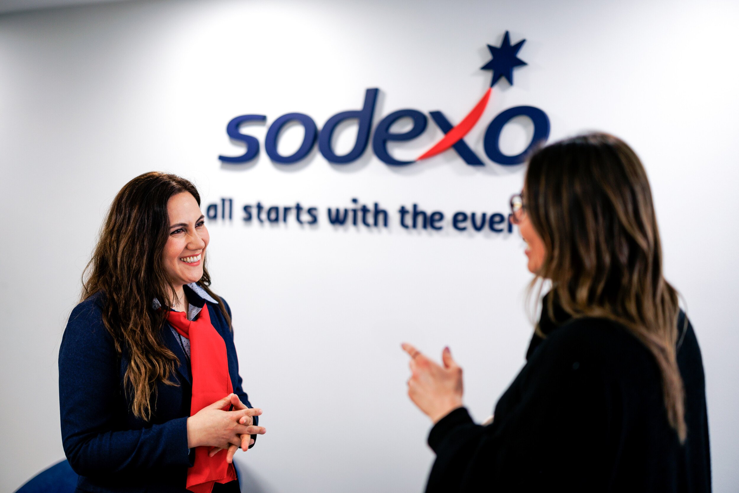 Due donne parlano davanti ad un muro con il logo Sodexo