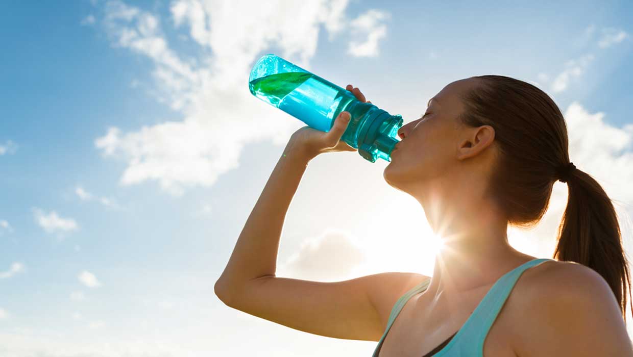 Donna beve dalla borraccia per idratarsi correttamente nei mesi più caldi
