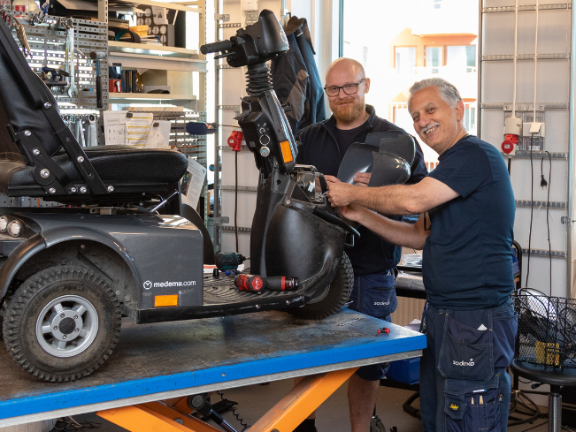Två medarbetare på hjälpmedelsservice gör underhåll på en permobil
