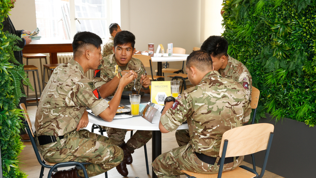 Four soldiers seating and eating around a table.