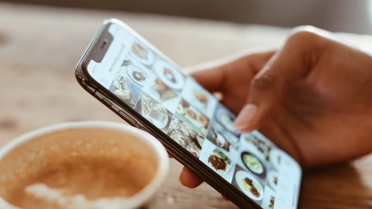 a close pic of a hand with a cell phone and a cup of coffee
