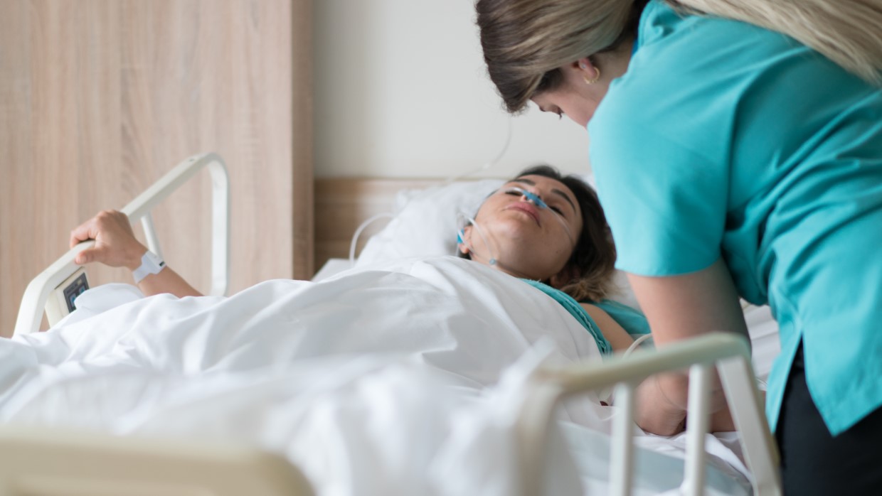 A healthcare professional aiding a patient lying in a hospital bed. 