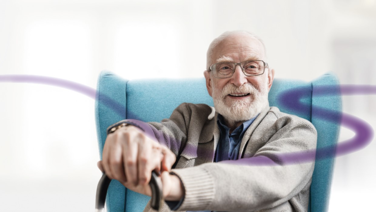 Older man sat in chair with walking stick looking content