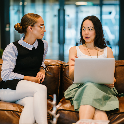 Two women talking in an office with one having a laptop with her