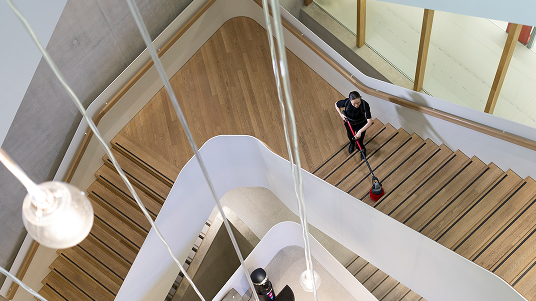 A person cleaning a large multi‑level staircase with a floor machine, viewed from above