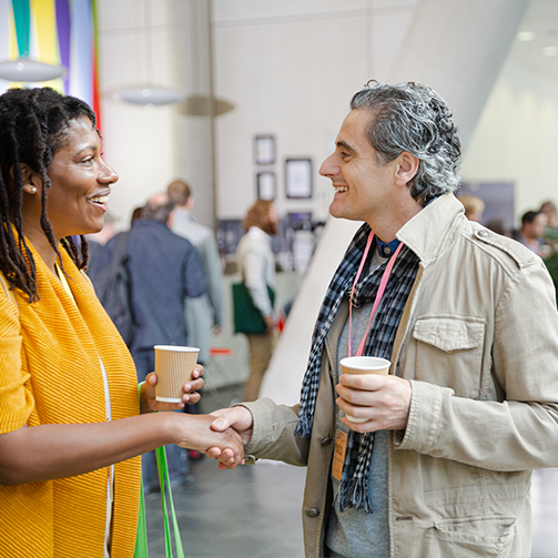 A man and woman shaking hands, both holding a coffee