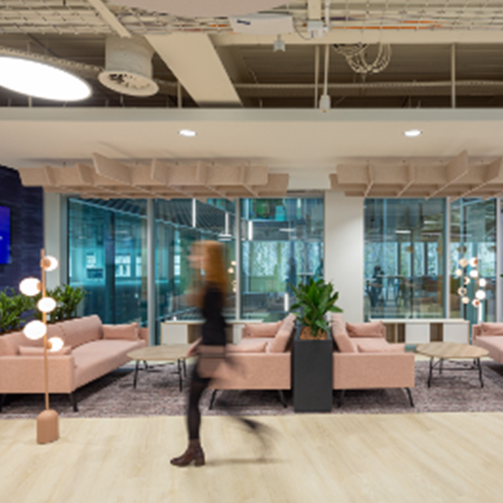 A woman walks through an office with a large glass wall, providing a transparent view of the workspace