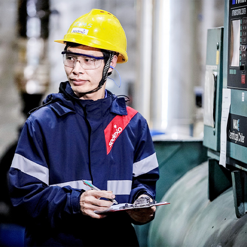 A man wearing a hard safety hat and a blue jacket inspecting