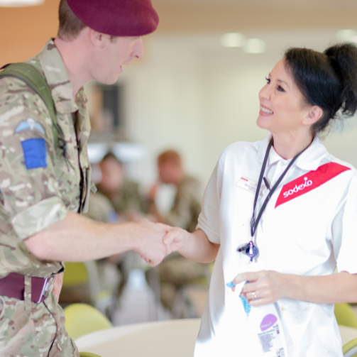 A Sodexo cleaner in a white uniform smiling and shaking hands with a military man