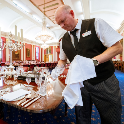 A man in a vest and tie arranging a table for a formal event