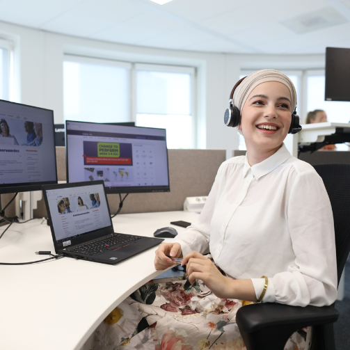 A woman in a headscarf sitting at a desk with two monitors 