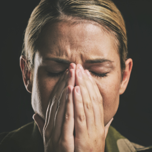 A female soldier in uniform with her hands covering her face