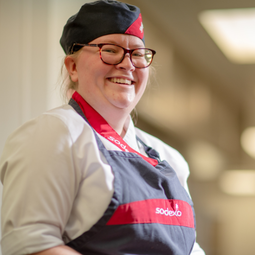 A woman with glasses and a red apron, smiling