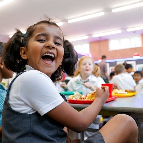 A young girl happily eating lunch in a school cafeteria