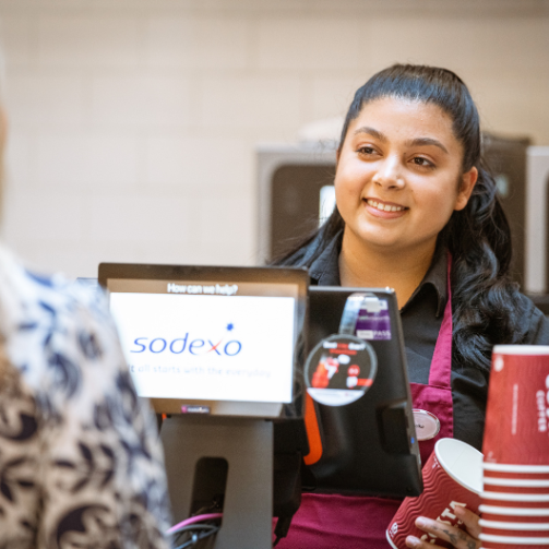A staff in an apron smiling behind a till
