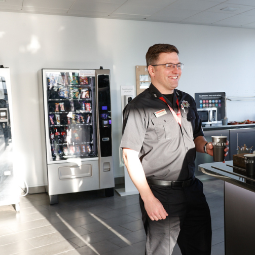 A smiling man in uniform standing in front of a vending machine