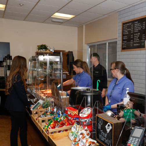 A suited woman standing by a food/snack station as uniformed staff attend to her