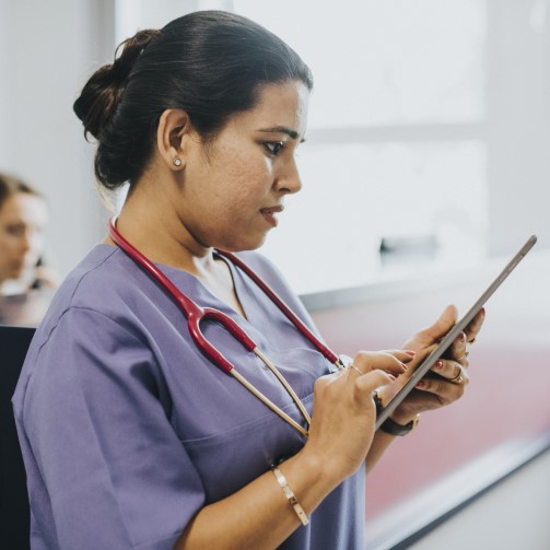 A nurse in scrubs using a tablet computer.