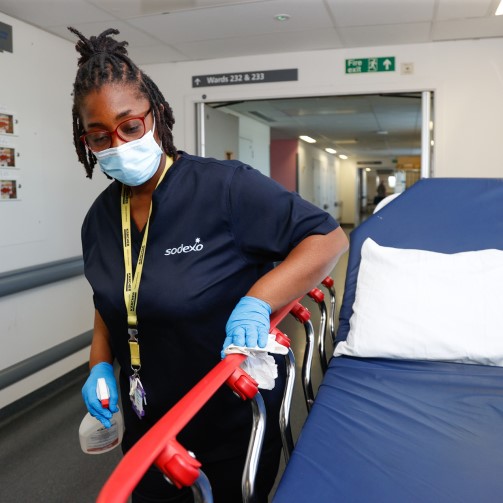 A member of the Sodexo team cleaning an empty bed in a hospital corridor before it is used on a ward