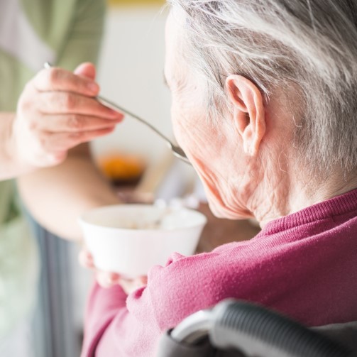 An elderly woman in a wheelchair being fed by a caregiver