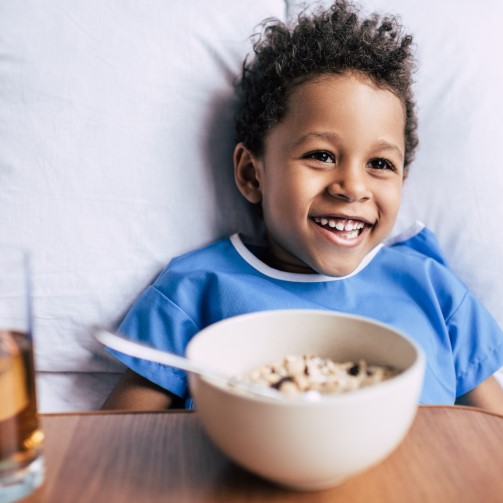 Smiling, happy young boy sat in bed with his breakfast cereal in front of him