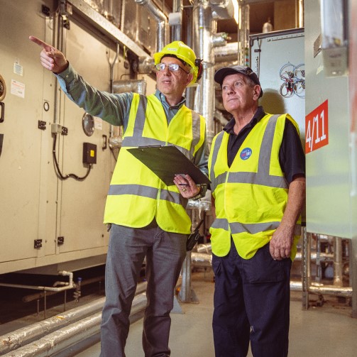 Two men in safety vests standing in front of a large industrial machine