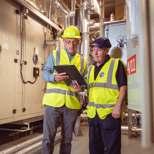 Two men in safety vests standing in front of a large industrial building