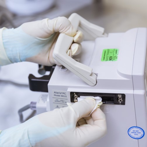 A pair of hands wearing white gloves are taking a swab from a medical equipment