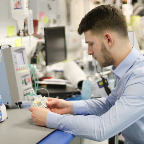 A man is sitting down at a table, fixing a clinical technology device