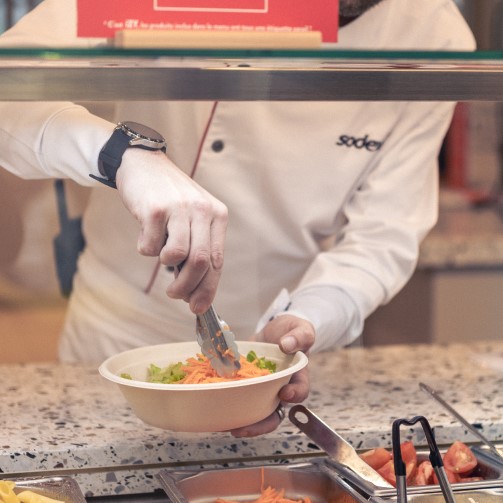 A chef serving up food from a buffet, holding a bowl and tongs