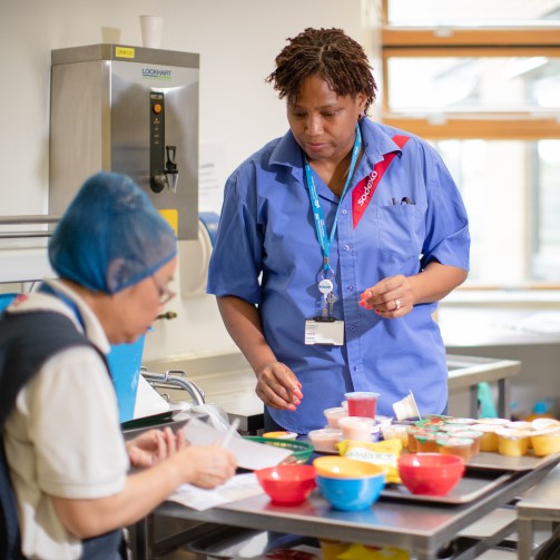 Two hospital kitchen workers are portioning food