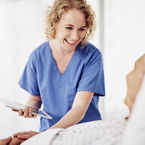 Female nurse holding a tablet is talking to a patient and holding his hand