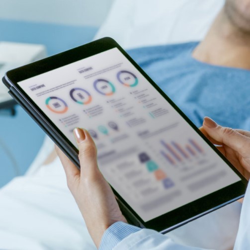 Hands of a staff member is checking patient data by the patient in hospital bed