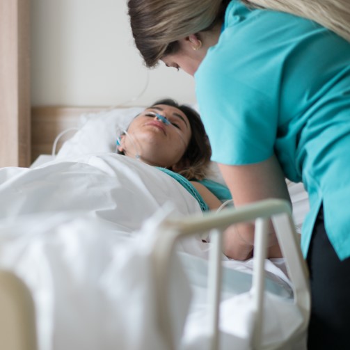 A patient is lying in a hospital bed with a nurse leaning over her
