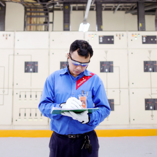 A worker wearing white gloves is taking notes in front of a large panel