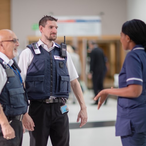 Two men in blue uniforms talking with a woman