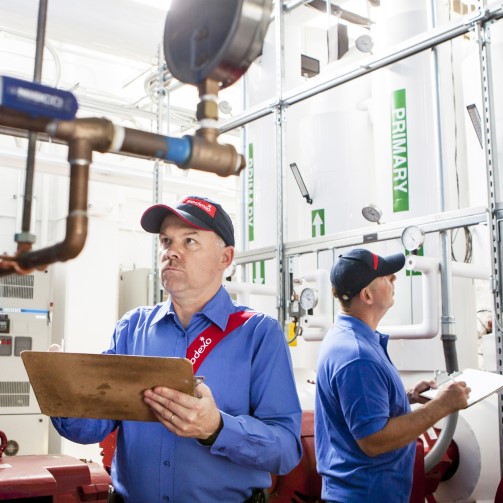 Two workers wearing uniforms and hats are taking notes