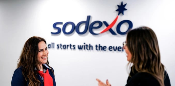 Two colleagues talking in an office with a blurred Sodexo logo in the background