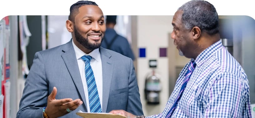 Two colleagues discussing work while holding documents in an office setting.
