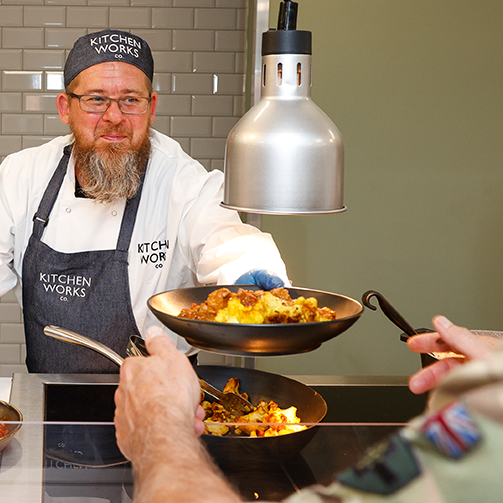 A man wearing a chef's hat serving a plate of healthy food