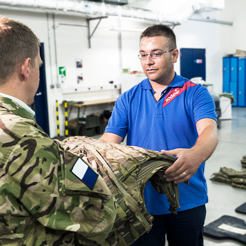 A man in a Sodexo's blue shirt delivering a piece of clothing to a military