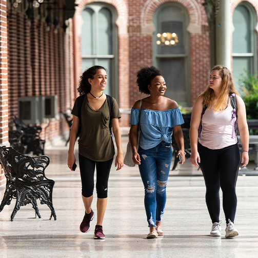 Three young women walking together in a courtyard, smiling and chatting