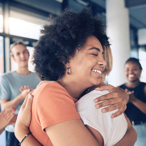 A woman warmly embraces another woman in an office