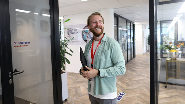A smiling man in office with a beard holding a laptop