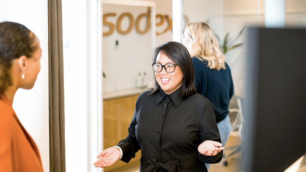 An east asian woman in a black shirt wearing glasses talking to a black woman in orange clothes