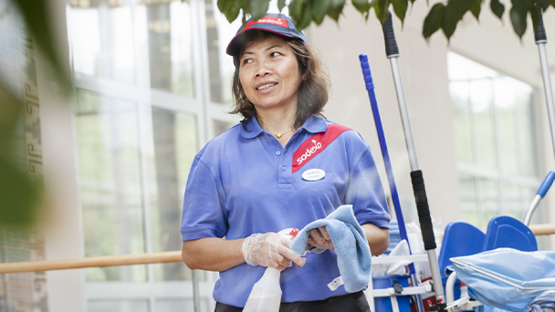 A woman in a Sodexo blue uniform and red hat holding a mop, ready to clean the floor