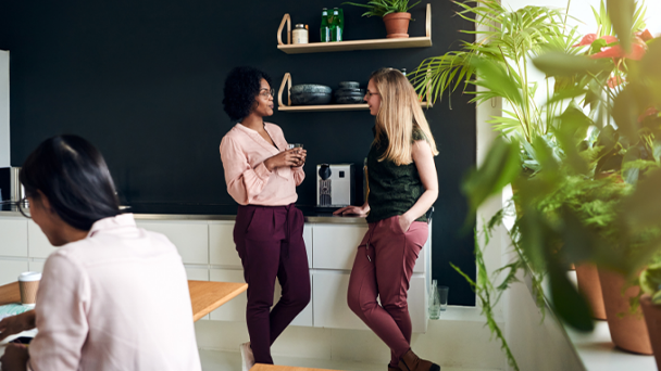 Two women chatting in a cozy kitchen, one stirring a pot on the stove while the other listens attentively