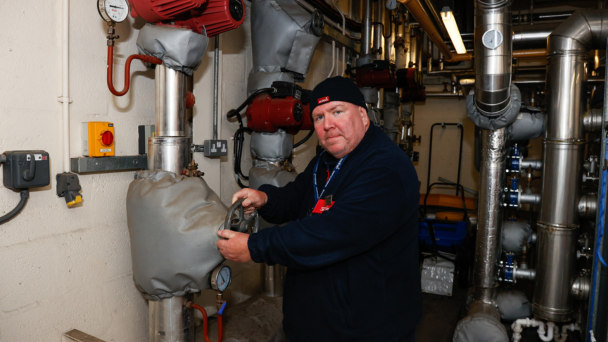 A man in a blue jacket repairing a pipe